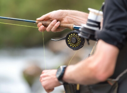 A man is holding a fly fishing rod and reel.