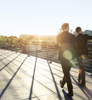 Two businessmen walking on a bridge at sunset.